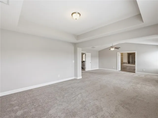 A spacious primary bedroom features tray and vaulted ceilings and plush carpeting, with access to a primary bathroom.