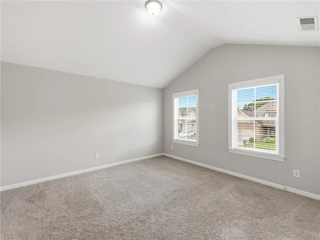 A spacious, naturally illuminated room boasts plush carpeting and a vaulted ceiling.
