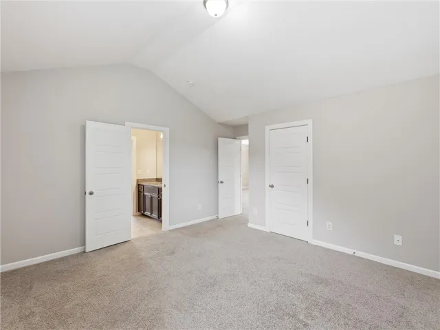 A spacious primary bedroom features soft carpeting, lofty vaulted ceilings, and a private ensuite entry.