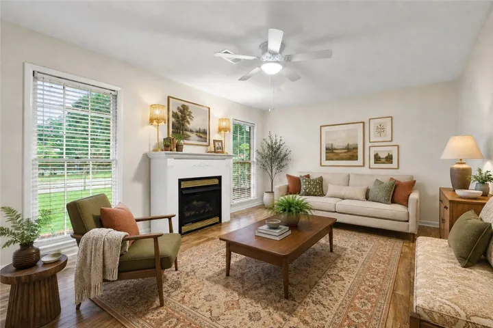 Warm wood flooring extends throughout this inviting living space, centered by a charming fireplace and bright windows. (Virtually staged)