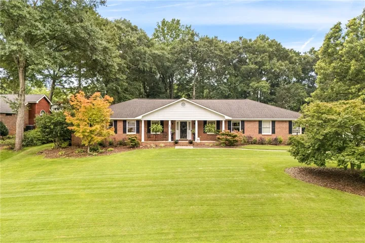 A classic brick ranch style home awaits, nestled amidst a spacious green yard and mature trees.