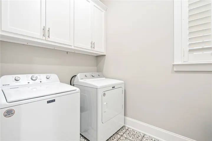 Bright laundry room features elegant patterned flooring and convenient upper cabinetry.
