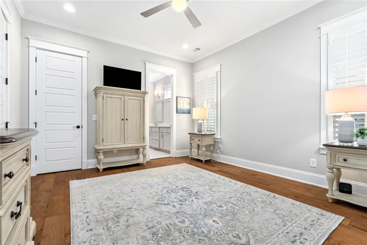 Hardwood flooring extends throughout this well-lit bedroom, offering seamless entry into an adjacent bathroom.