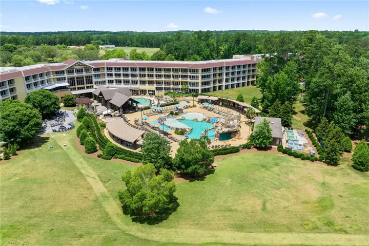 An aerial perspective reveals a vast resort pool with surrounding lounges, all nestled beside a lush green lawn.