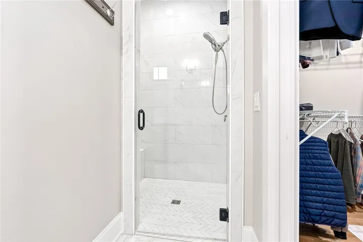 A sleek, tiled shower with a glass enclosure stands adjacent to a functional walk-in closet.