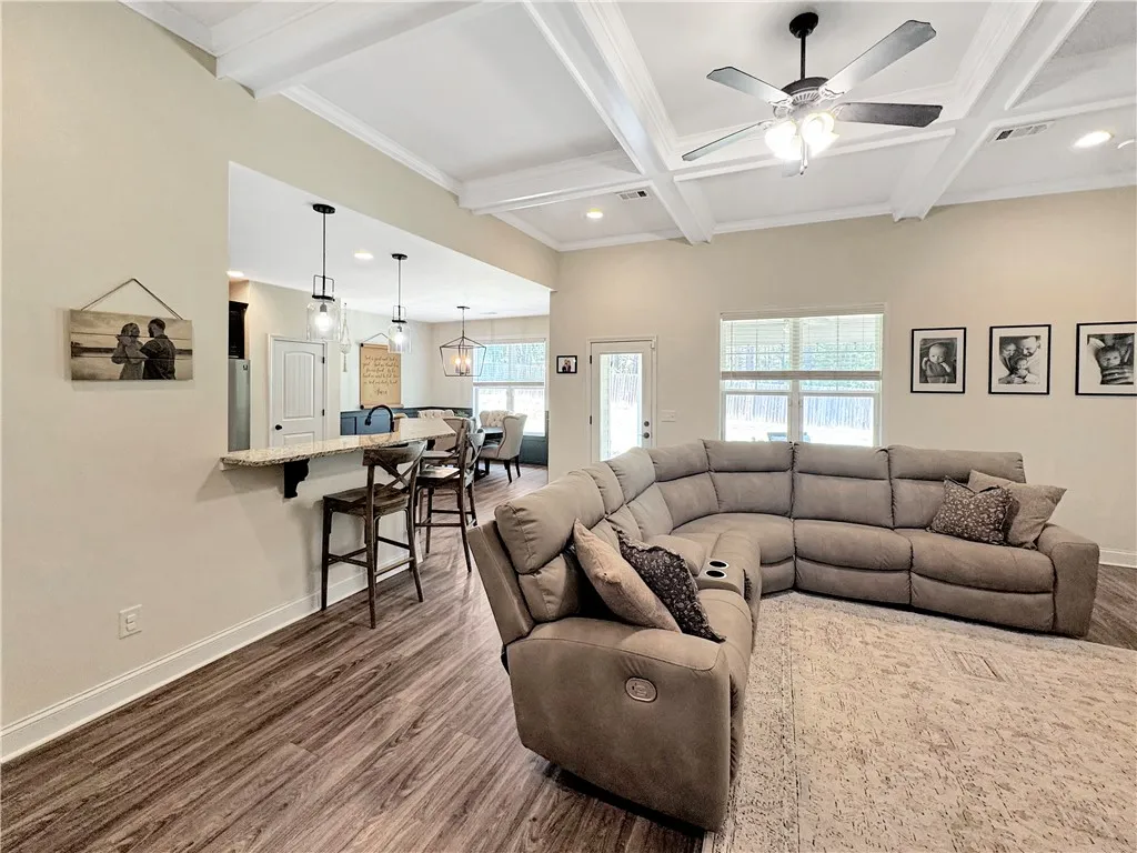 An open-concept great room with coffered ceilings and rich wood flooring flows seamlessly into the kitchen area.