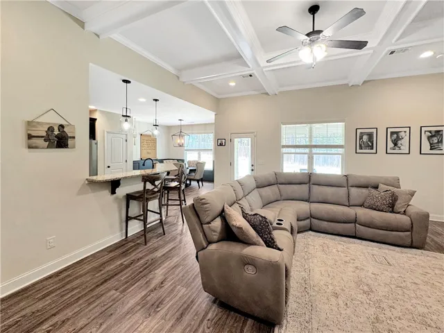 An open-concept great room with coffered ceilings and rich wood flooring flows seamlessly into the kitchen area.