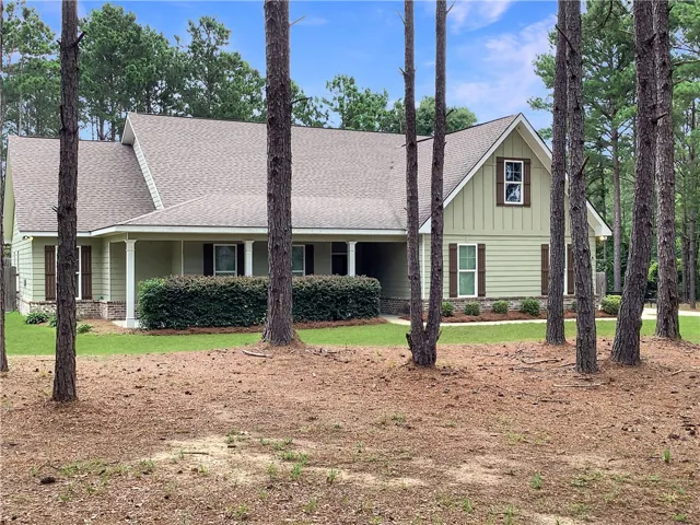 A classic exterior with a welcoming covered porch, enveloped by mature pine trees and well-maintained shrubbery.