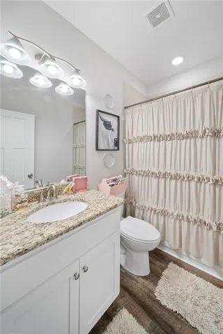 A well-appointed bathroom features a single vanity with a granite countertop and dark wood-look flooring.