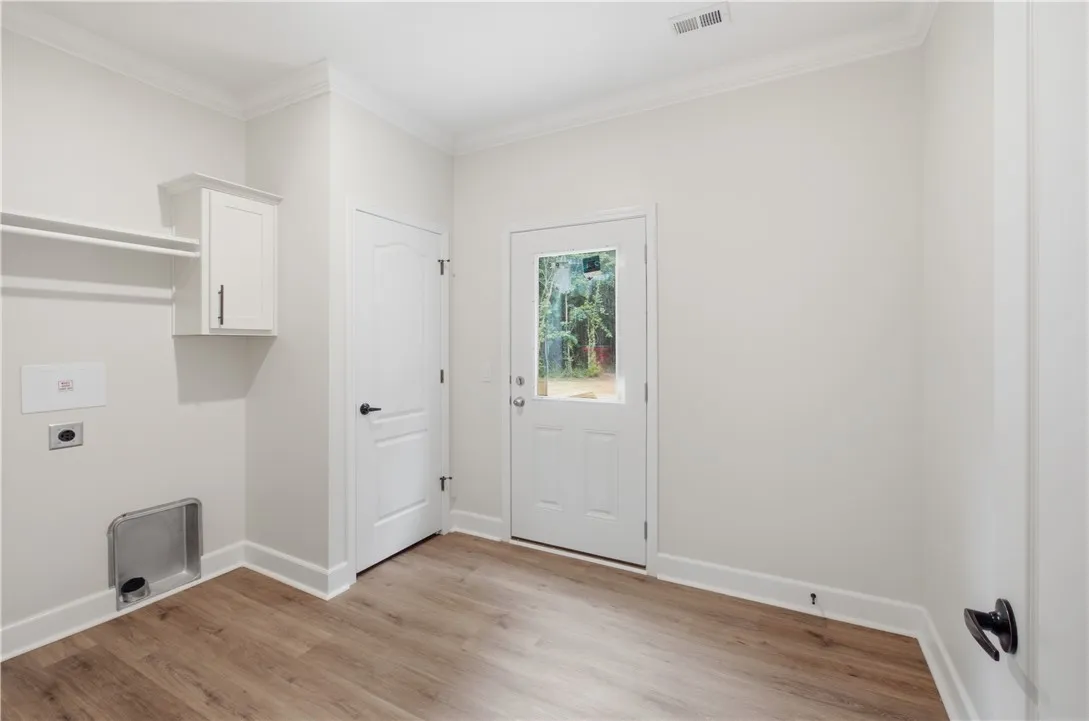 Functional laundry space featuring durable wood flooring and ample natural illumination from the glass-paneled door.