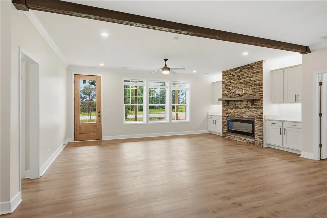 A spacious living area with abundant natural light, showcasing rich hardwood flooring and a prominent stone fireplace.