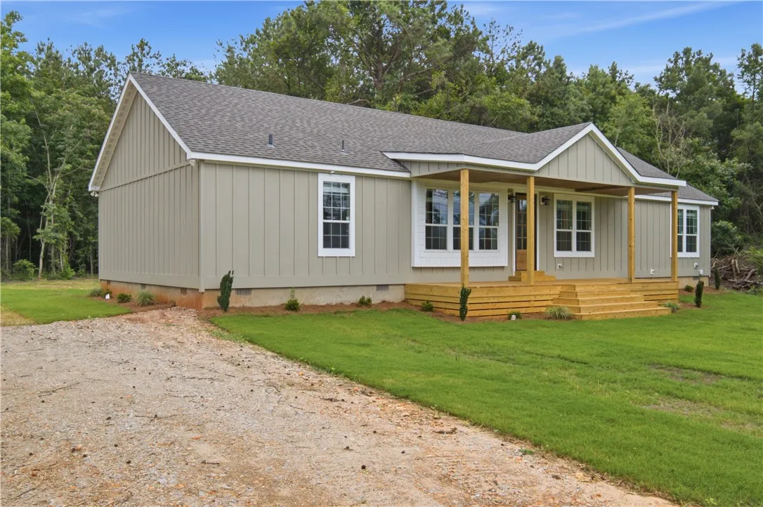 A newly constructed residence nestled amidst verdant trees offers a spacious front porch and ample outdoor area.