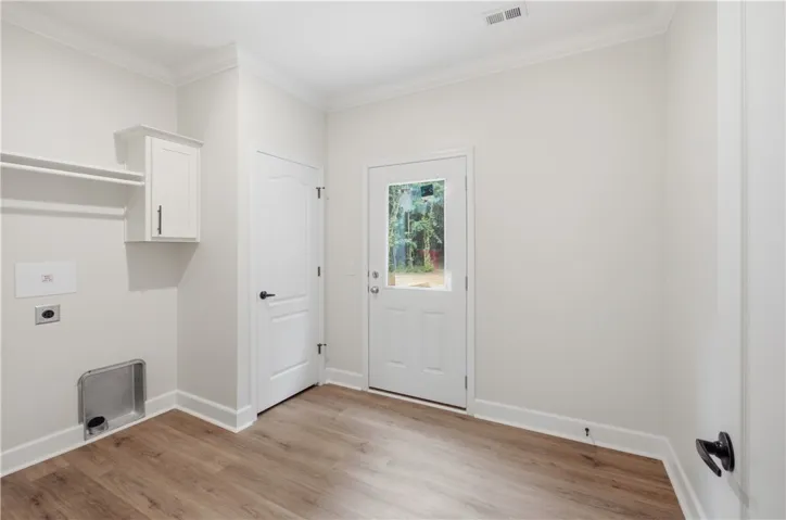 Functional laundry space featuring durable wood flooring and ample natural illumination from the glass-paneled door.