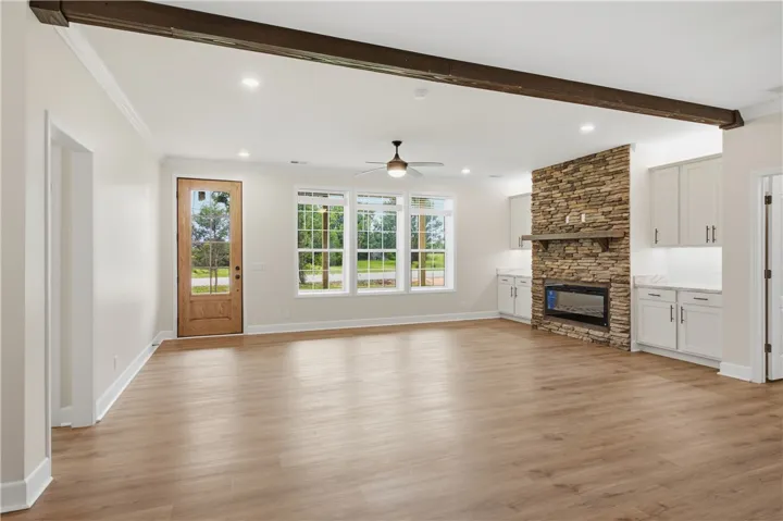 A spacious living area with abundant natural light, showcasing rich hardwood flooring and a prominent stone fireplace.