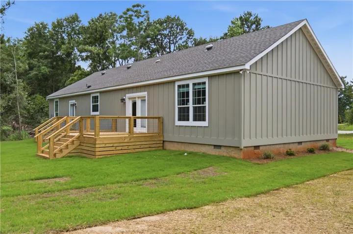 A new build with modern siding and an inviting wooden deck, set against a backdrop of lush trees.