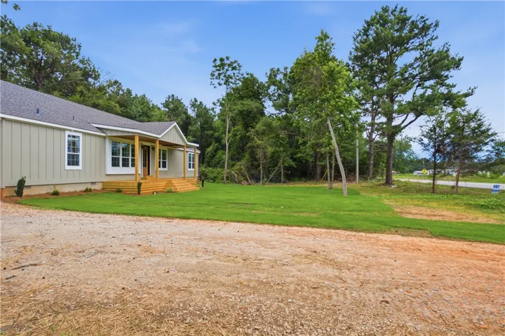 A welcoming front porch extends across the facade of this light-colored siding home, nestled amidst mature trees.
