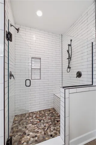 A well-lit shower features pebble flooring and crisp subway tile, creating a refreshing bathing space.