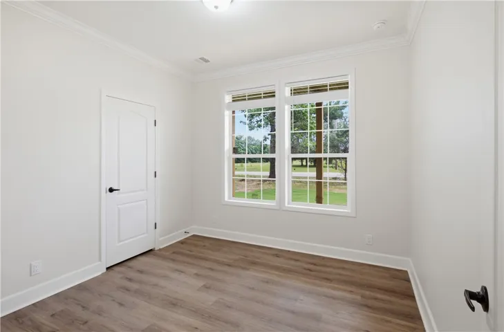 A well-lit bedroom features sturdy hardwood flooring and crisp white crown molding, offering tranquil views of the outdoors.