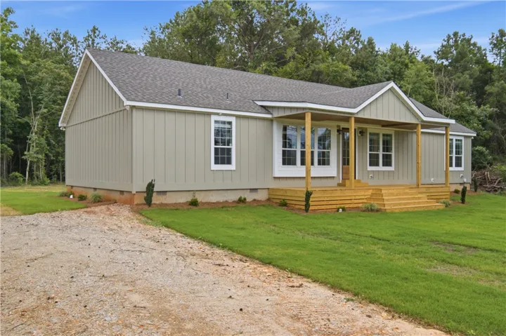 A newly constructed residence nestled amidst verdant trees offers a spacious front porch and ample outdoor area.