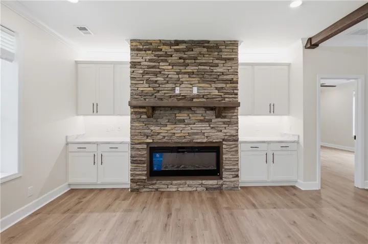 A striking stacked stone fireplace commands attention, flanked by elegant white cabinetry and warm wood flooring.