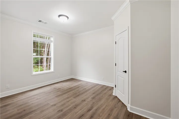 A well-lit room showcases durable laminate flooring, crisp white trim, and a window offering a lush, wooded view.