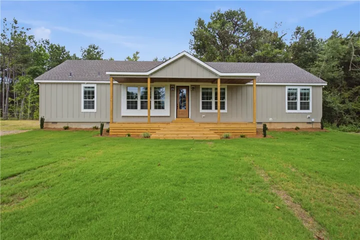A welcoming wooden front porch extends the length of this modern home with a lush lawn.