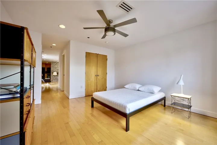 Blonde hardwood flooring anchors a well-lit bedroom, offering clear sightlines into the home's open-concept layout.
