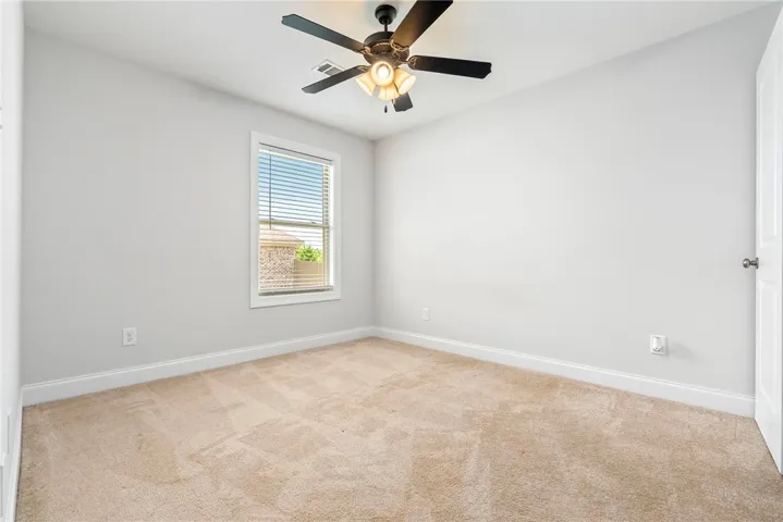 A well-lit bedroom with soft carpeting and a ceiling fan offers comfortable living.