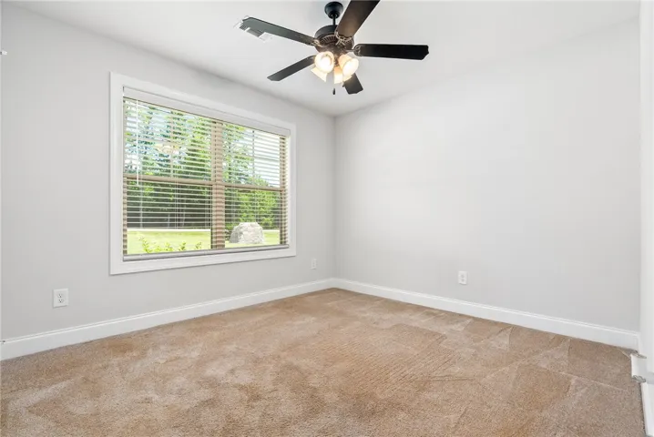 An airy bedroom offers a view to green outdoors, complete with a practical ceiling fan.