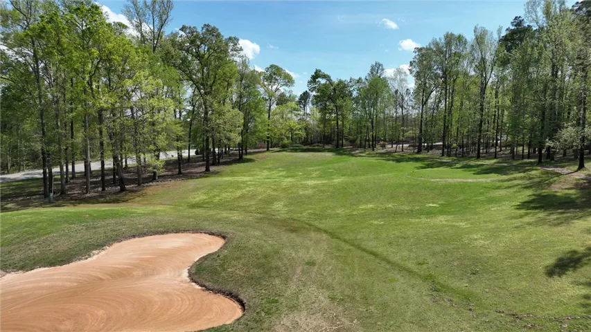 A verdant golf course with a sand trap, bordered by a dense forest under a clear sky.