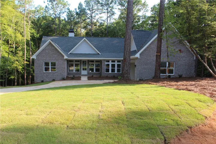 A newly constructed brick home with a spacious driveway and attached garage, nestled among mature trees on 1 acre lot