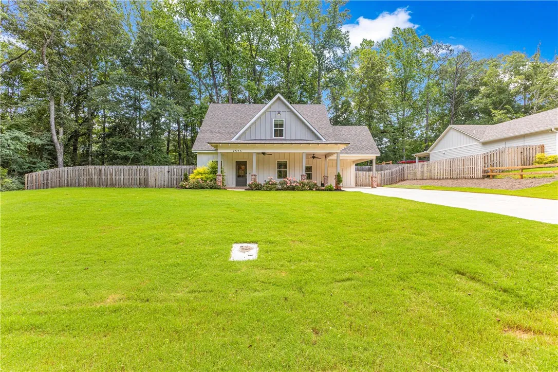A charming cottage-style residence nestled among mature trees, boasting a welcoming front porch and an expansive, verdant lawn.