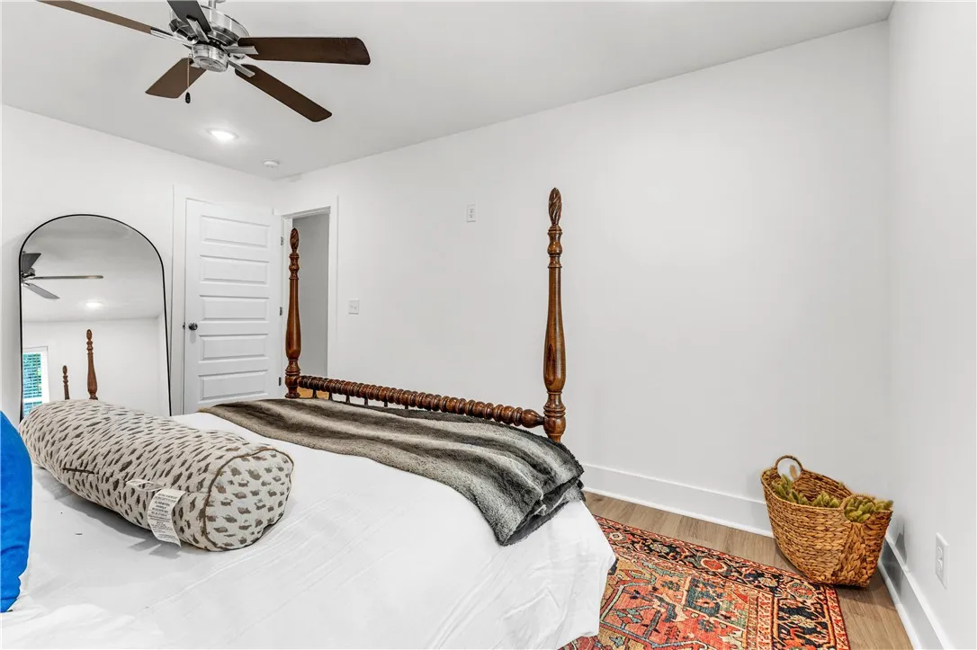 A well-lit bedroom with smooth white walls and rich hardwood flooring, topped with a modern ceiling fan.