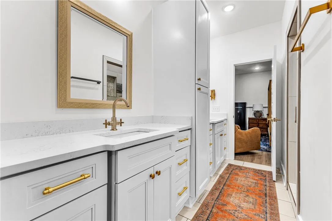 A well-appointed bath features crisp white cabinetry, quartz counters, and elegant brass fixtures.