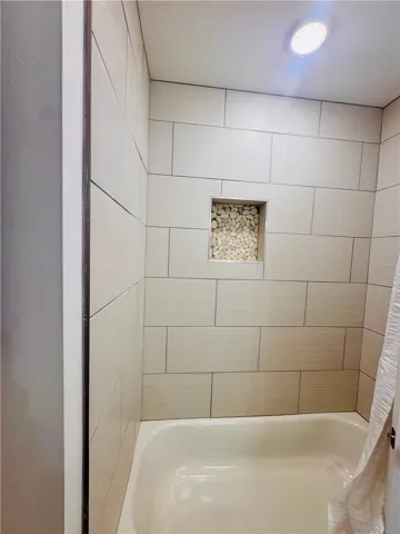 Clean lines define this pristine bathroom, featuring a well-lit shower area with a unique stone-accented niche.