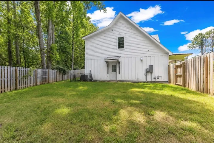 A private, grassy yard featuring a white siding structure and natural wood fencing.