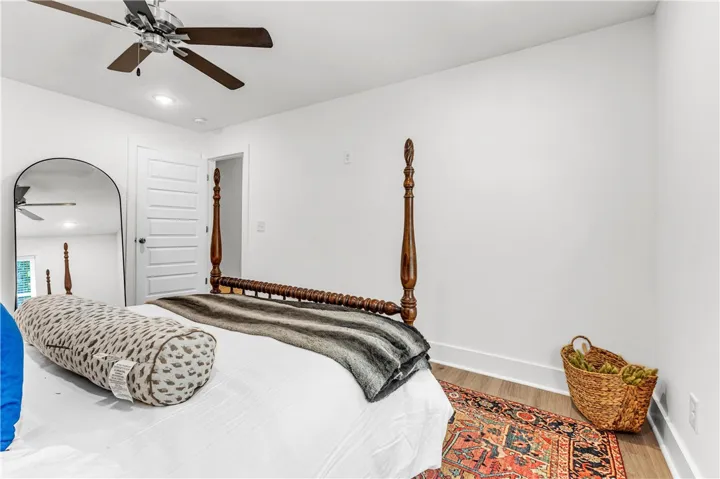 A well-lit bedroom with smooth white walls and rich hardwood flooring, topped with a modern ceiling fan.