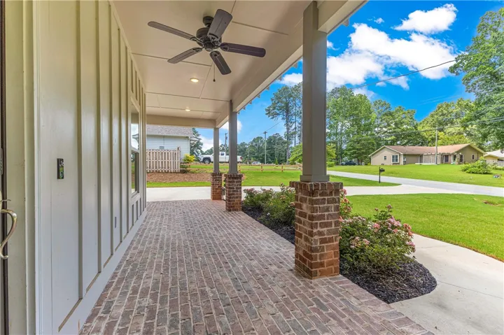A welcoming brick-paved front porch with sturdy brick columns and a ceiling fan.