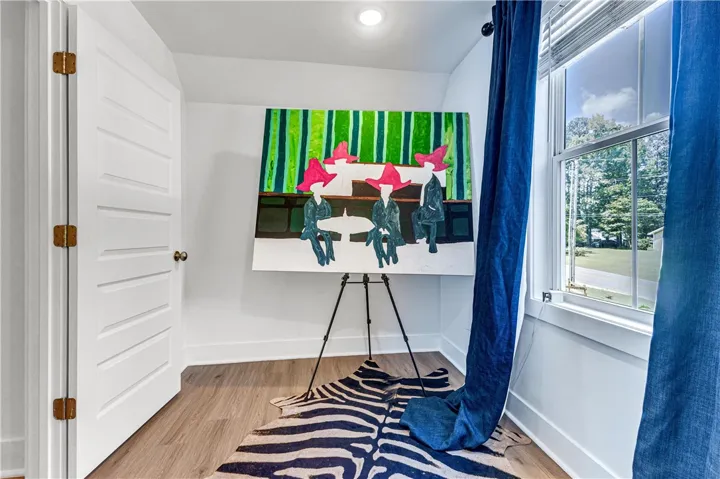 An inviting room boasts bright wood-look flooring and a window with verdant outdoor views.