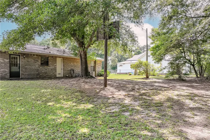 A verdant lawn sprawls towards a charming brick dwelling, shaded by mature trees.
