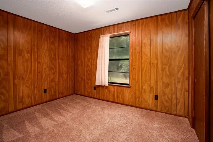 A quaint, naturally illuminated bedroom awaits customization with its warm wood paneling and soft carpet.