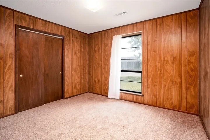 Wood-paneled walls and soft carpet define this cozy, well-lit bedroom.