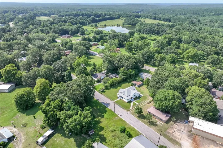 An aerial panorama reveals a classic residence nestled amongst mature trees, with verdant landscapes stretching to a tranquil pond.