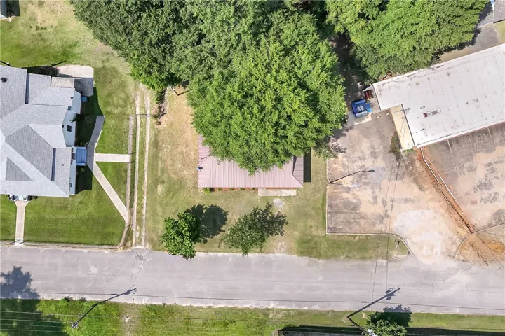 An aerial perspective reveals a private structure nestled among mature trees, bordering a paved road.