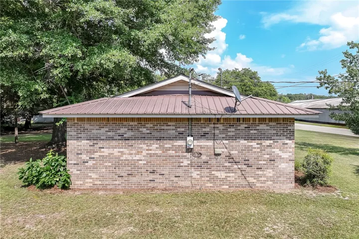A durable metal roof crowns this robust brick structure, set amidst mature trees and a clear blue sky.