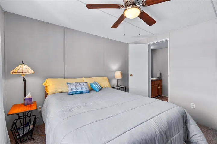 The cozy bedroom features a ceiling fan, plush carpet, and convenient access to a private bathroom.