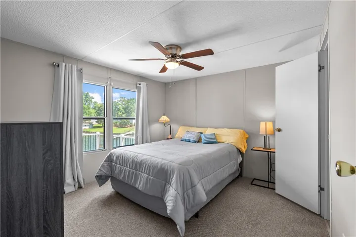 Lake views from a well-lit bedroom featuring a ceiling fan and carpeted floors.