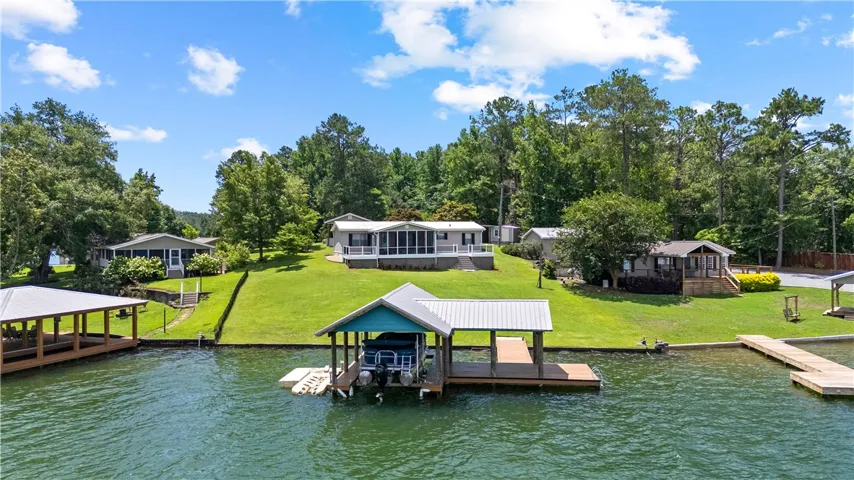 A boat dock extends into a pristine lake, with a charming lakeside home nestled amongst verdant trees.