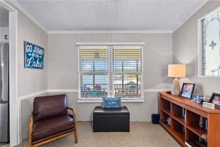 A well-lit sitting area with a captivating lake view through horizontal blinds, featuring wainscoting and crown molding.