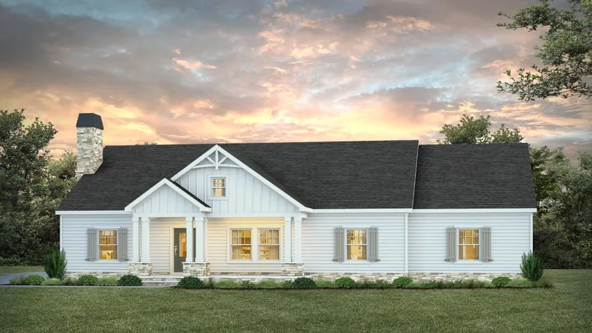 A charming white ranch home with a striking stone chimney sits nestled against a dramatic sunset backdrop.